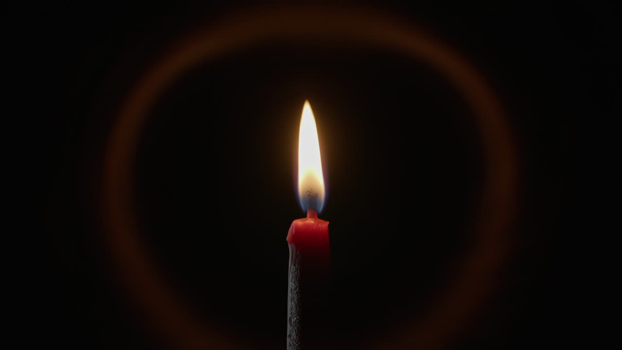 Oddálení plamene svíčky s jemnou září na černém pozadí. Vosková svíčka hoří.
