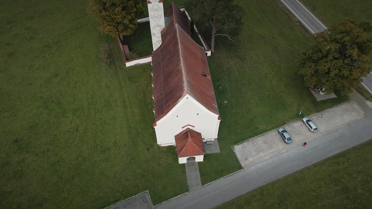 Movimento suave de drone 4K em recuo acima da Igreja de São Coloman em Schwangau, afastando-se para revelar os terrenos da capela, prados e estradas rurais que se cruzam