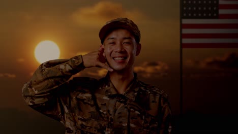 close up of asian man soldier smiling and making call me gesture to camera while standing with flag of the united states, sunset time