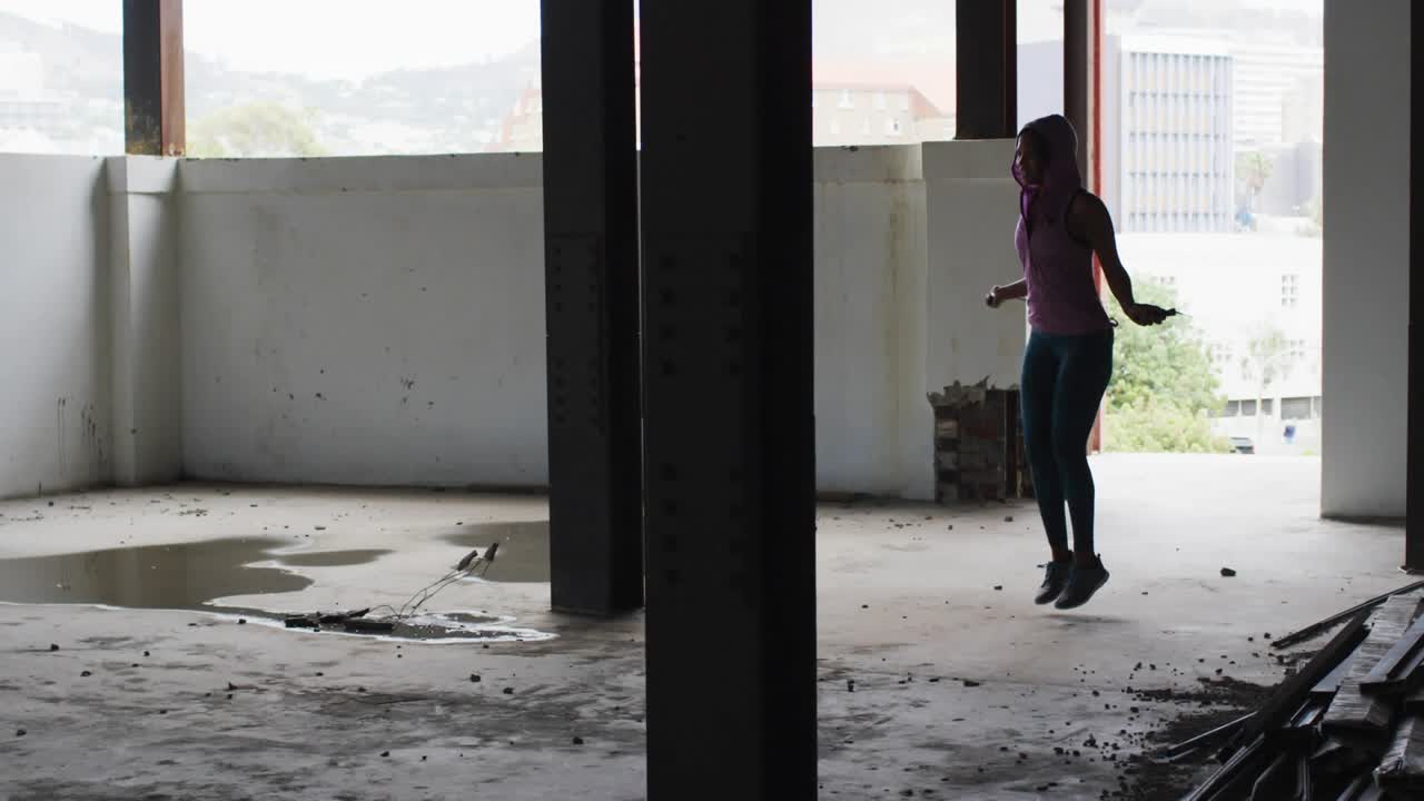 Fitness woman starting skipping rope near column, creating floating emoji overlays, holding phone