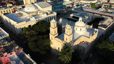 cámara aérea al atardecer deslizándose hacia la derecha y levantándose detrás de los campanarios de la rectoría jesús en merida, yucatan, mexico