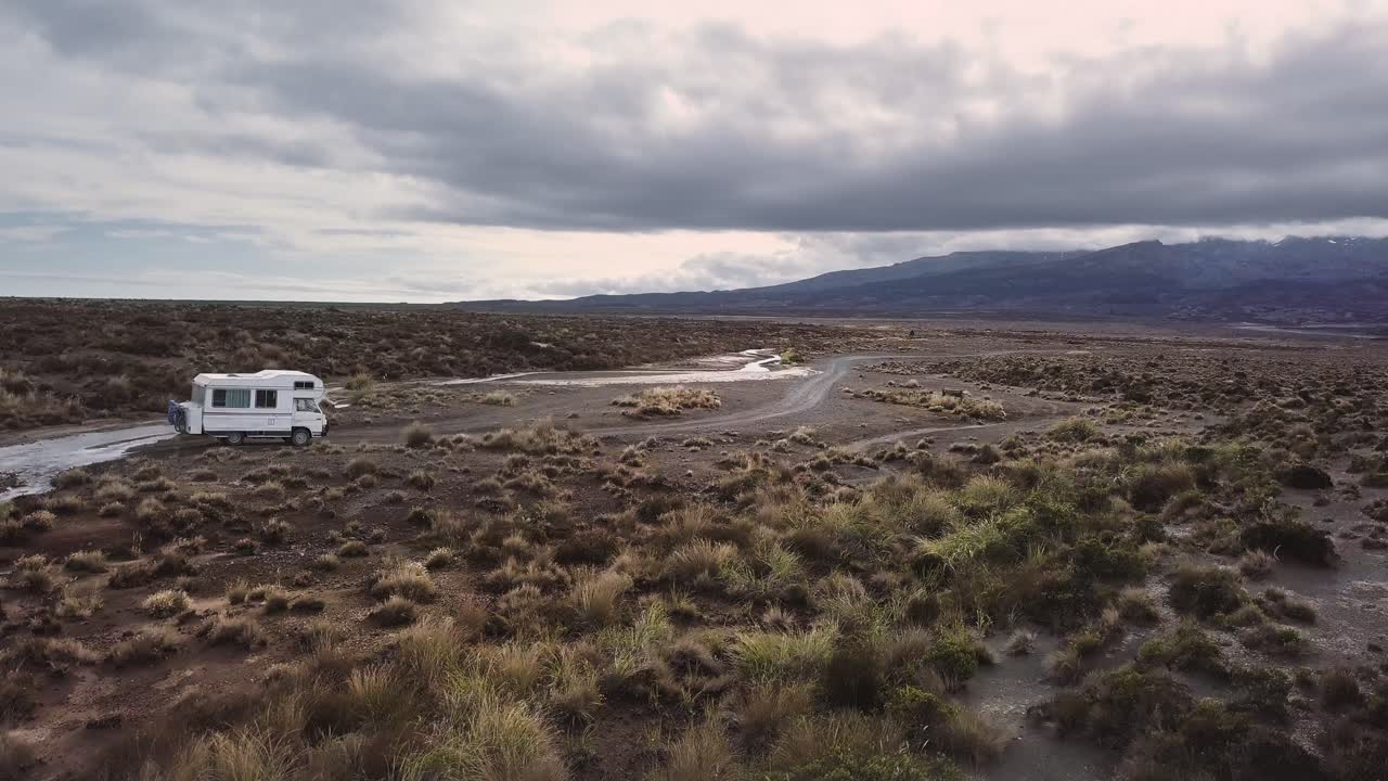 An old camper van drives through the desert and crosses a small creek at Tukino Access Road, Tongariro National Park - Rangipo Desert.