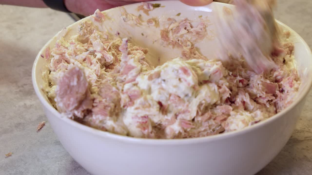 Close-up view as chef mixes salmon salad ingredients in white bowl