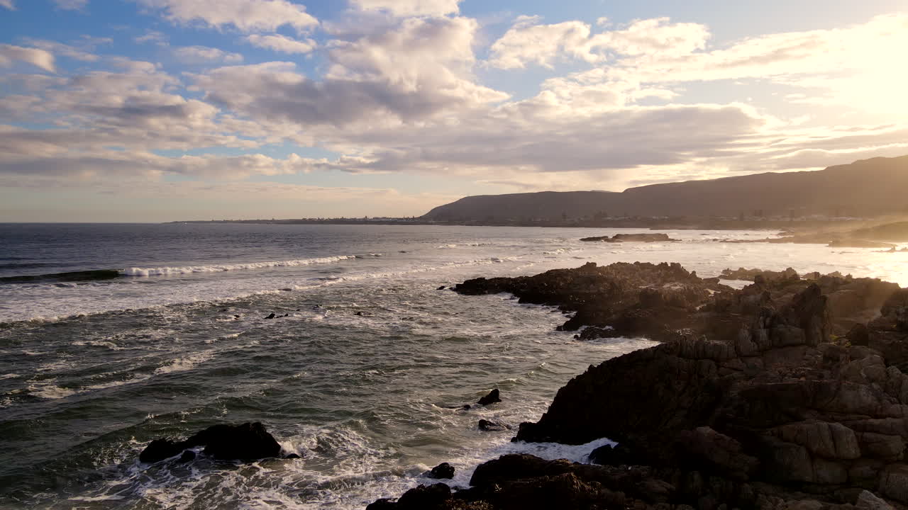 Luftfoto fra stigende drone av en mann ved solnedgang på den taggete kystlinjen ved Hermanus som ser ut over havet