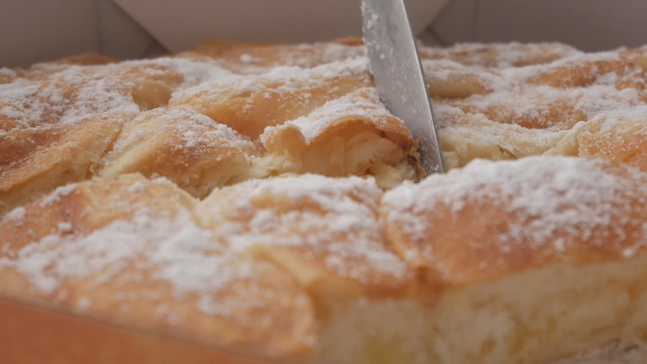 Fluffy golden-brown Ensaimada from Menorca being sliced, dusted with powdered sugar