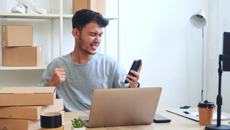 young indonesian entrepreneur celebrates good news on phone while working on laptop