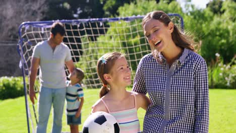 portrait of smiling mother and daughter standing with football