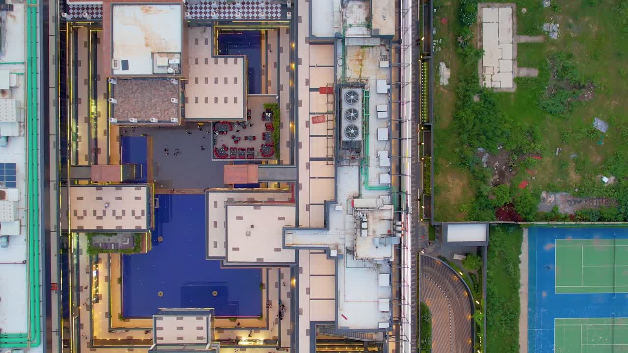 Aerial drone side moving straight down shot over sports complex and busy shopping mall with water feature outdoor seating and solar panels and HVAC on roof