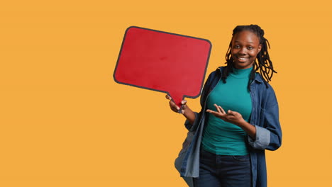 smiling woman holding red speech bubble sign, studio background