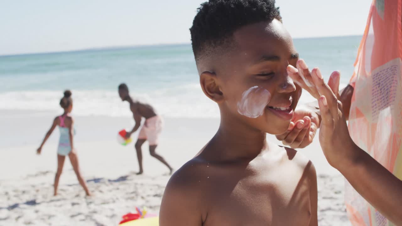 Smiling african american family using sun cream on sunny beach