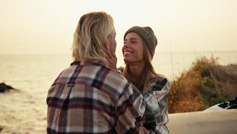 close-up shot of a blonde girl in a green hat in a checkered shirt examines her blond boyfriend and holds him by the neck tenderly and kisses him while sitting on a bench on the sea strawberries during sunrise in the morning in summer