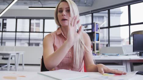 Caucasian-businesswoman-having-video-chat-going-through-paperwork-in-modern-office