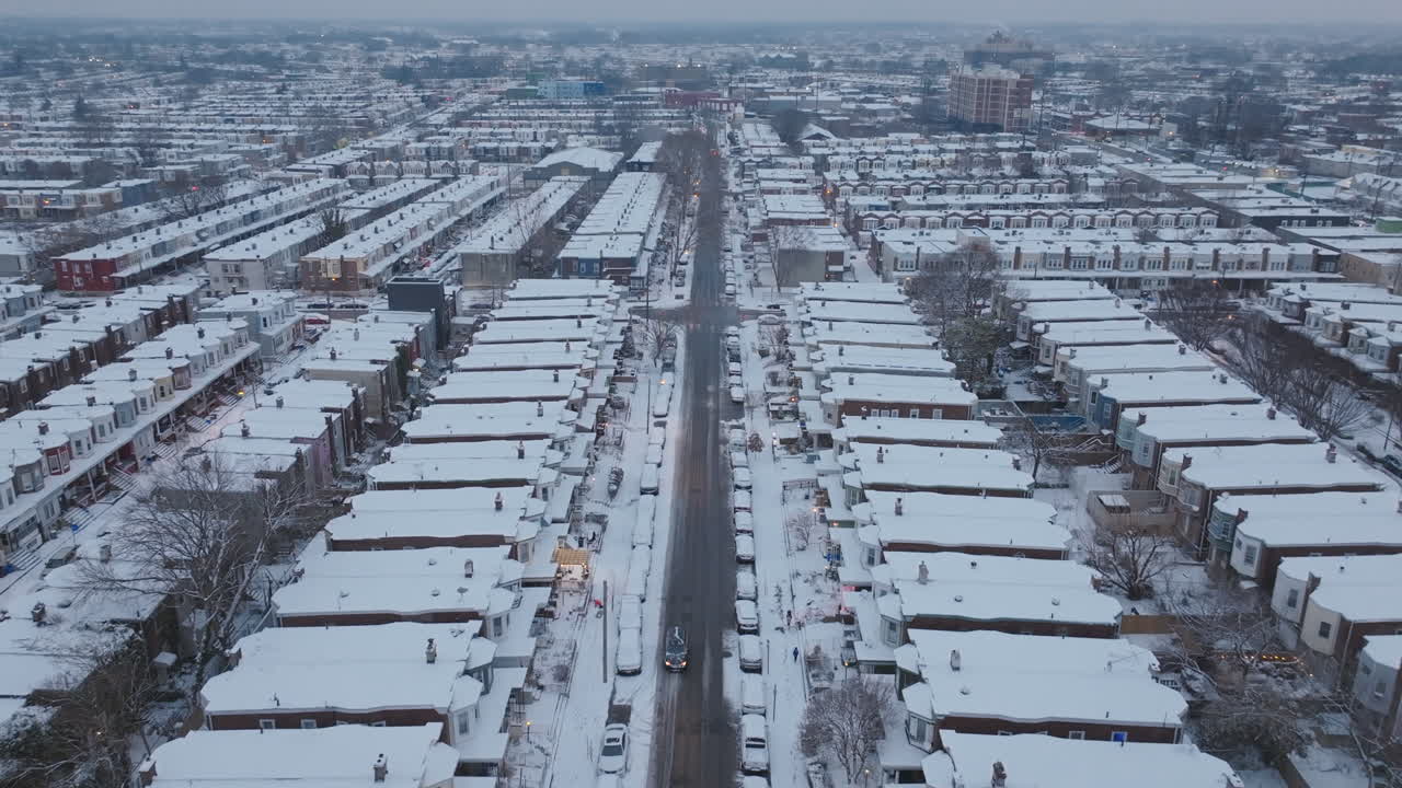 Aerial drone footage flying down a street of historic row homes in snow covered neighborhoods in West Philadelphia, Pennsylvania as cars drive down deserted streets.