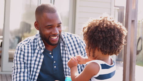 Young-black-girl-blowing-bubbles-with-dad-outside-house