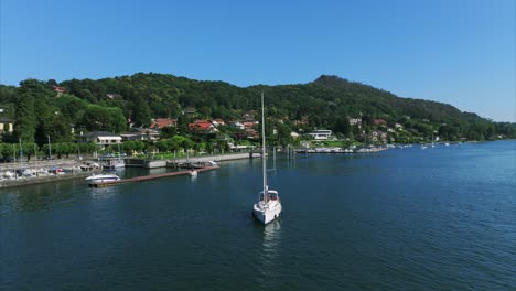 Aerial-View-Of-A-peaceful-sailboat-glides-on-a-clear-lake-surrounded-by-a-picturesque-hillside-town,-embodying-tranquility-and-the-scenic