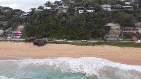 Drone-Volando-Desde-El-Océano-Hacia-La-Playa-Y-Un-Acantilado-Que-Muestra-Casas-Caras-En-El-Acantilado