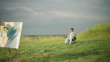 in a tranquil grass field, a woman in a white dress focuses intently on painting a canvas with a palette in hand, while a man in a black hat and checkered shirt sits in a chair nearby