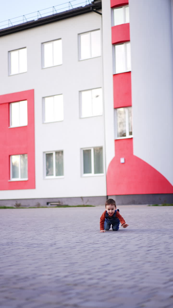 Baby boy crawls on all four by the tiled ground outdoors. Kid approaches camera stopping in the midway. Vertical video.