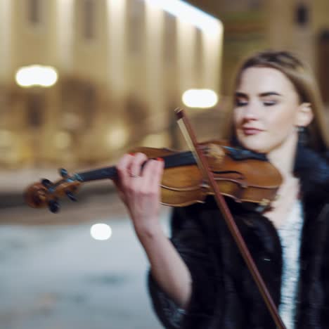 a student of musical faculty in an evening dress and coat is playing a famous music on violin on the background of the monument and city buildings behind her. close-up