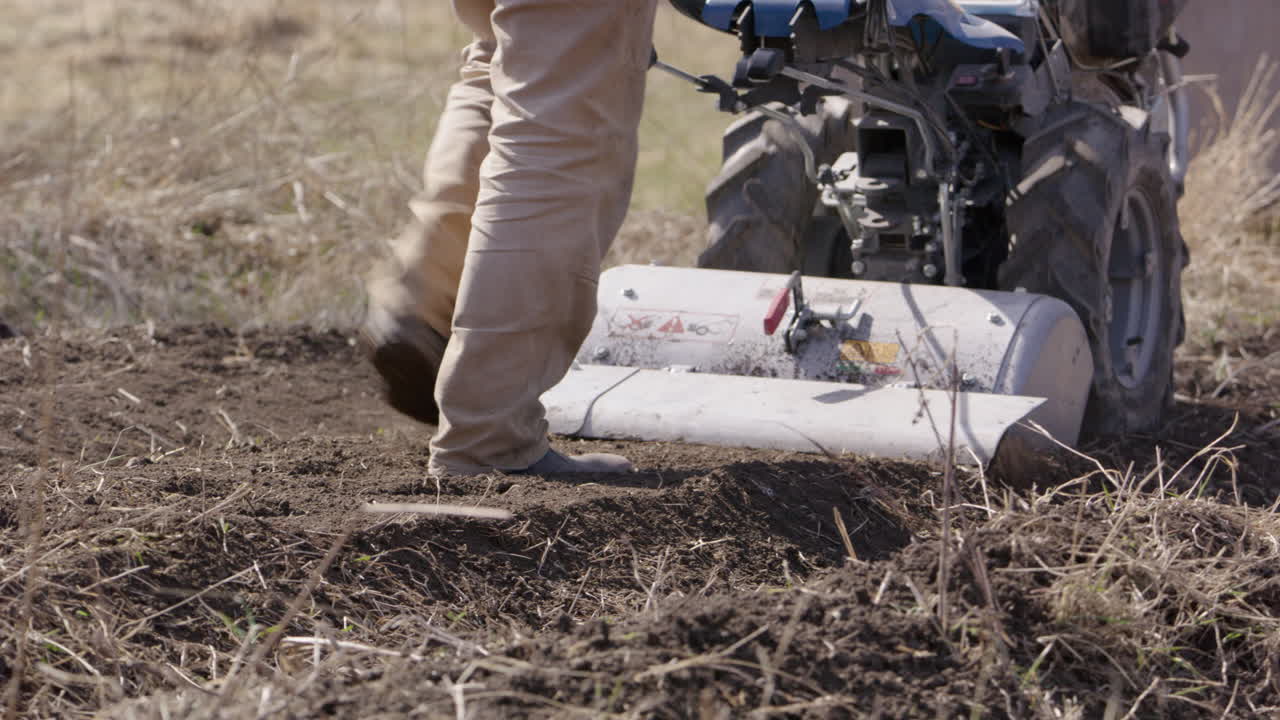 hombre empujando un motocultor, trabajando la tierra en suecia, agricultura, plano medio