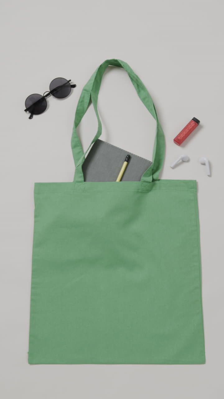 Vertical video of green bag with sunglasses, notebook and lipstick, copy space, slow motion