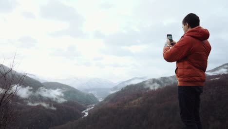 man taking photo of snowy mountain valley