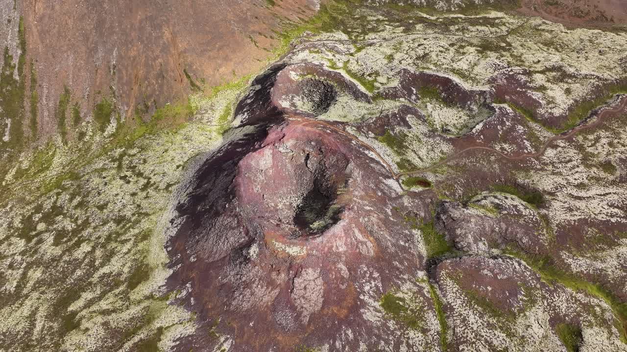 Drone liitää Eldborg-kraatterin yllä paljastaen pyöreän tulivuorikartion, tummanpunaisen laavamaaston ja näyttäviä, muinaisista purkauksista muodostuneita geologisia kuvioita Islannin Reykjanesin alueella.