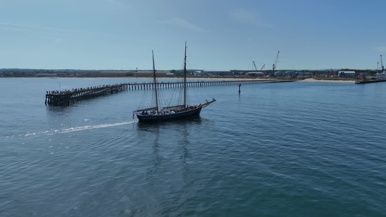 Boat with tall masts sailing into industrial harbour