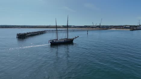 boat with tall masts sailing into industrial harbour