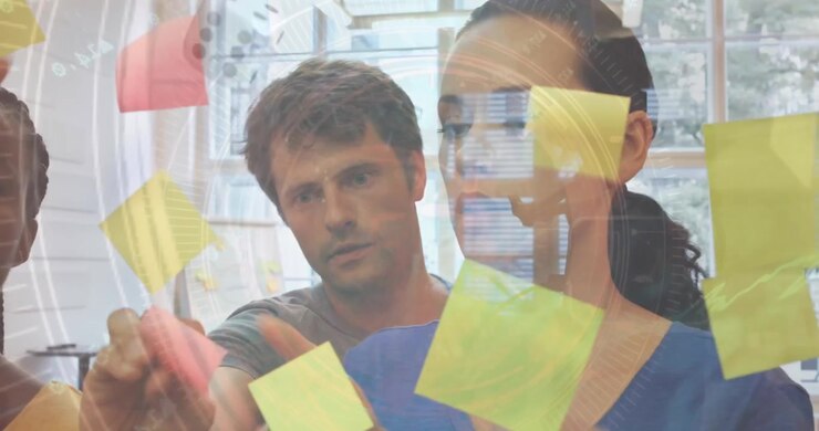 Elaborazione dati su colleghi d'ufficio caucasici (uomo e donna) che attaccano post-it su una lavagna di vetro