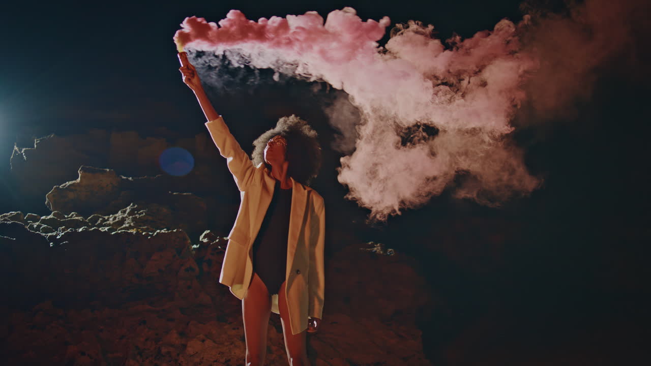 Activist waving colorful bomb at night outdoors. Confident woman under smoke