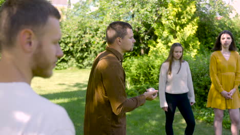 side view of caucasian young man throwing a petanque ball in the park on a sunny day while his friends wait their turns