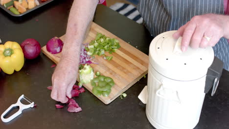 Midsection-of-senior-caucasian-couple-cleaning-vegetable-peels-in-kitchen-at-home,-slow-motion