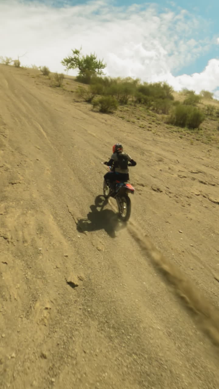 el motociclista monta el vehículo en una colina arbustiva con un dron fpv. el piloto fuerte y hábil en casco conduce al pico de la montaña en carreras extremas. el motocross en las tierras altas