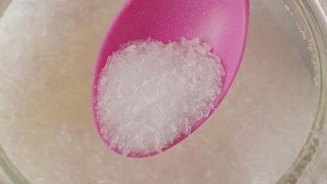 primer plano de una cuchara rosada que recoge cristales blancos de glutamato monosódico