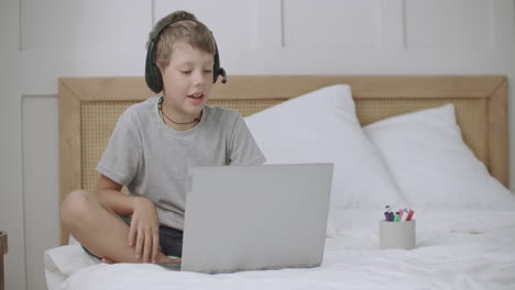 teen-boy-is-coloring-and-drawing-pictures-at-album-lying-on-bed-at-home-and-communicating-by-laptop