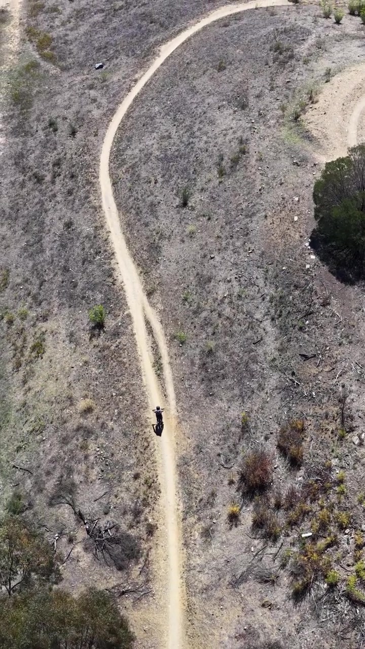 Ripresa aerea con drone di un ciclista che percorre un sentiero tortuoso nella boscaglia a Canberra.