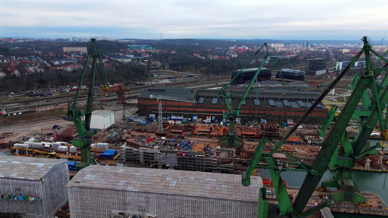 Aerial ascend above Gdansk Shipyard, cranes, ship construction, and warehouses with open buildings and heavy equipment