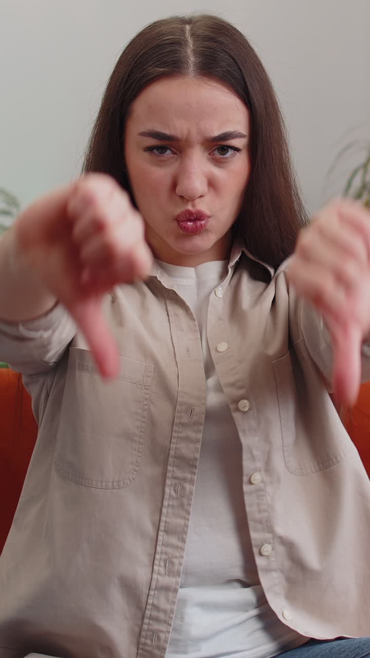 Upset young woman showing thumbs down dislike bad work disapproval dissatisfied feedback at home