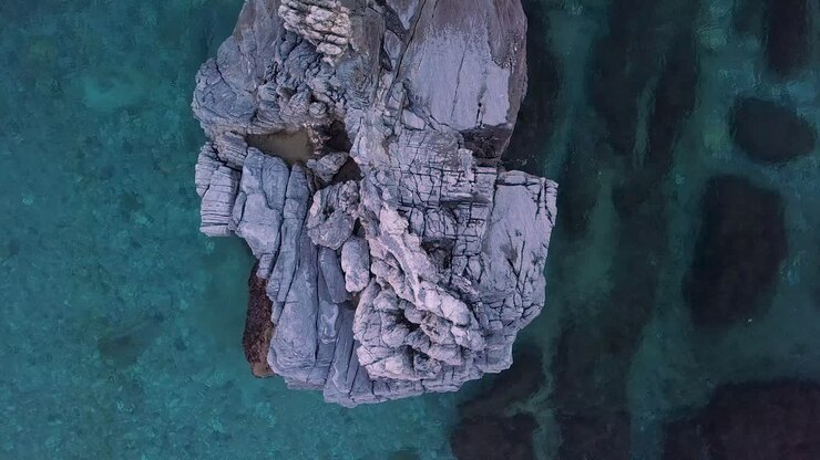 Ripresa zenitale statica con drone 4K di una grande roccia nelle acque cristalline del mare