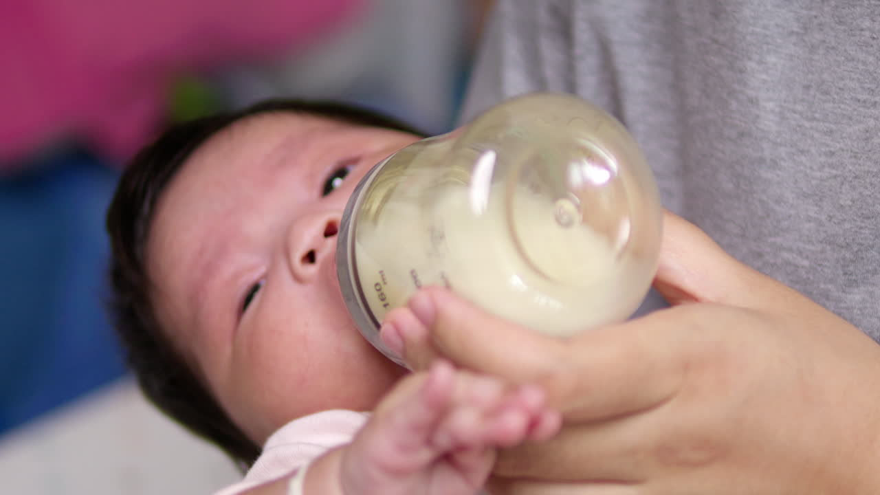 Cradling her newborn child in her arms while feeding her some formula milk in a plastic feeding bottle.