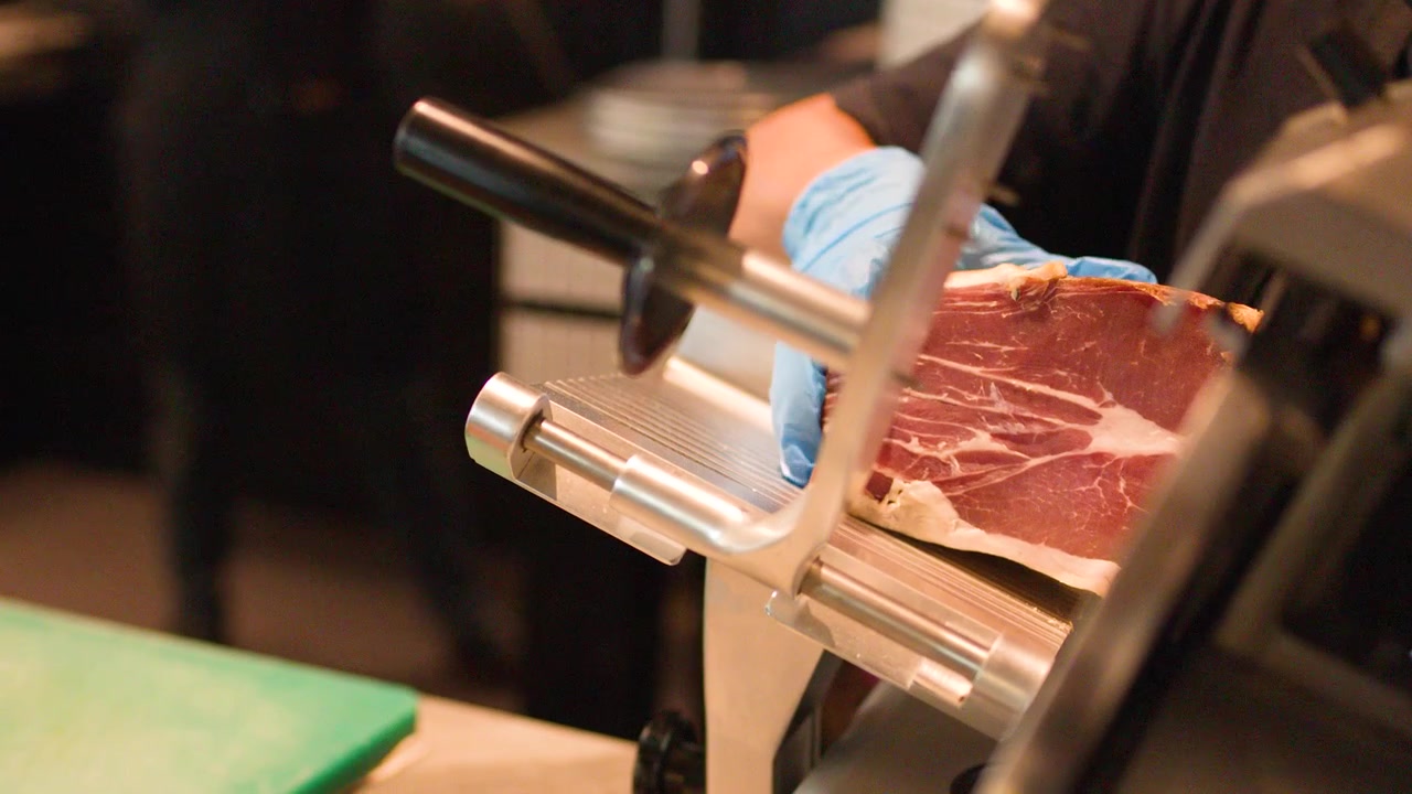 Chef che affetta prosciutto su affettatrice professionale