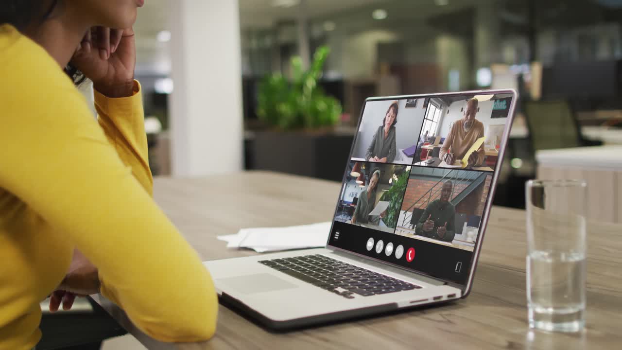 Biracial woman using laptop for video call, with diverse business colleagues on screen
