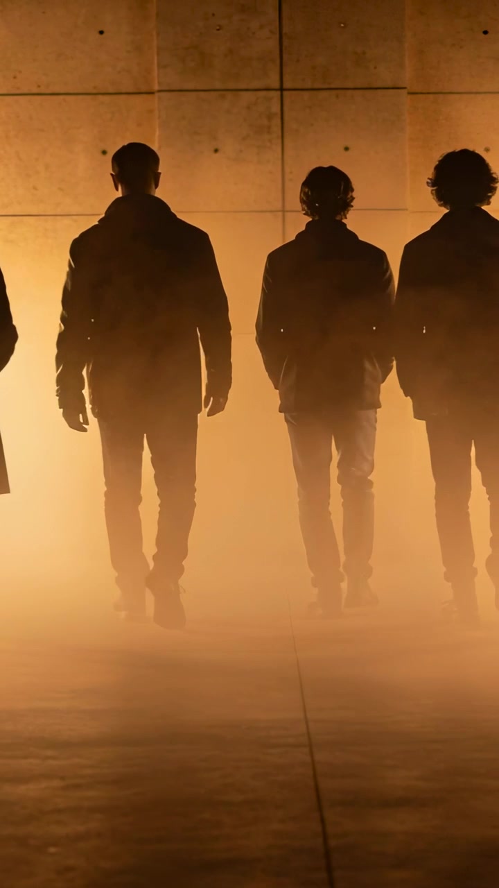 Vertical video: Walking on cue 3 men wearing coats stepping toward warm light in concrete hall, fog