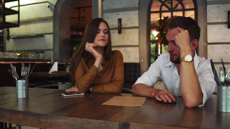 ein schönes paar sitzt zusammen in einem restaurant. sie trinkt tee und schaut sich eine speisekarte an, während ihr freund versucht, essen für sie auszuwählen. er gibt ihr auch essen-ratschläge.