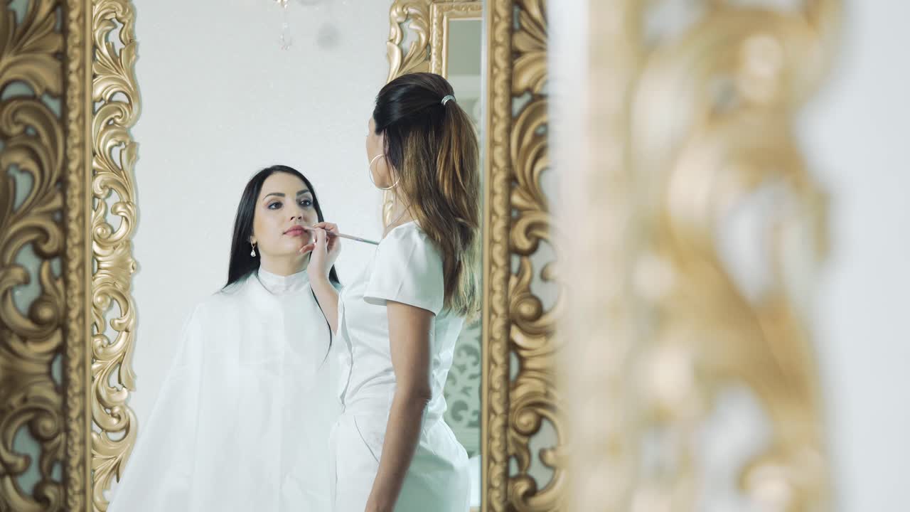 Beautician paints lips with a red pencil to a young girl in a beauty salon. Permanent makeup procedure
