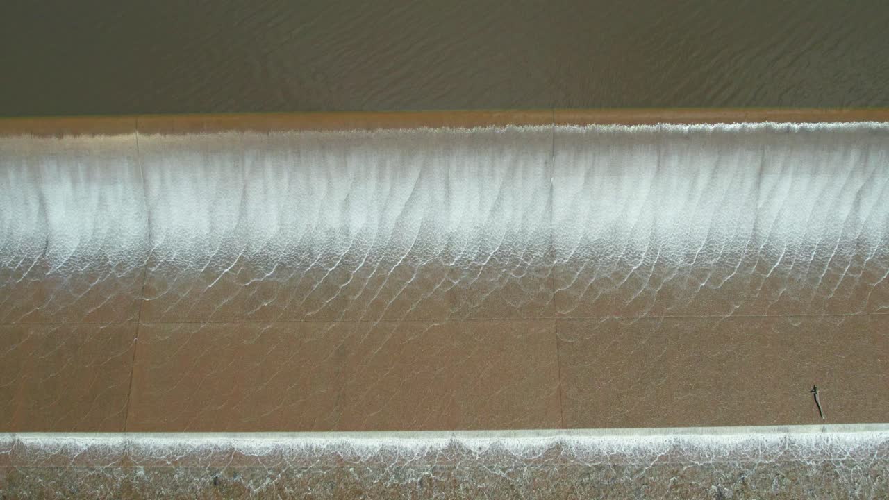 Close up then rising aeial view of water spilling over the Upper Coliban Reservoir spillway, central Victoria, Australia