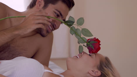 man tickling his girlfriend with a red rose on bed