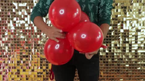 Mann-Bindet-Vier-Rote-Latexballons-Mit-Goldenem-Hintergrund-Zusammen