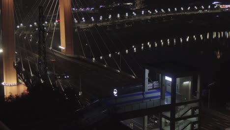 a city bridge at night in chongqing, with sparse vehicle traffic and a pedestrian below wearing a raincoat and dancing